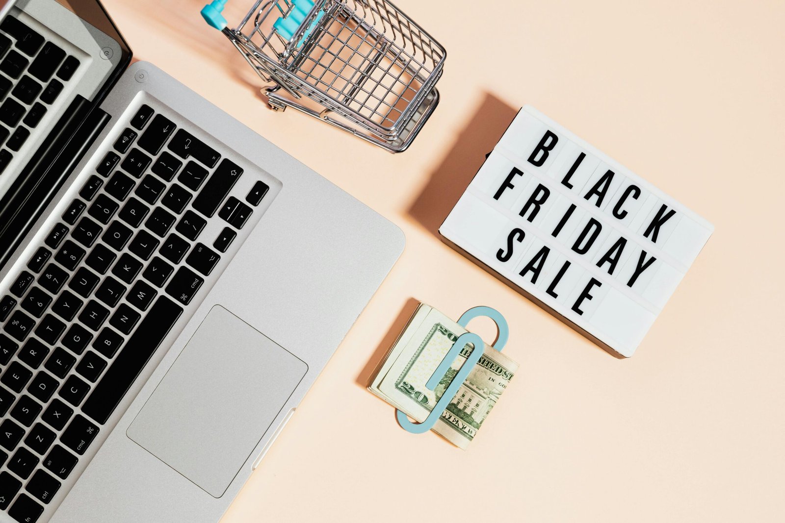 Overhead view of shopping cart, laptop, cash, and Black Friday sale sign.
