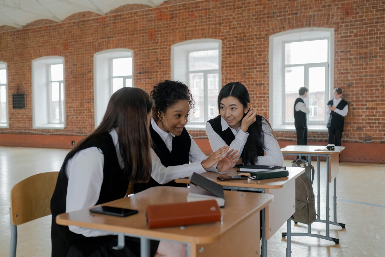 Diverse students in uniforms engaging in a classroom discussion with brick wall background.
