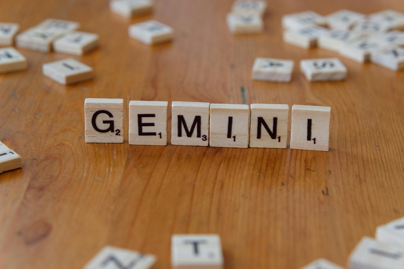 Gemini zodiac sign spelled with Scrabble tiles on a wooden table.