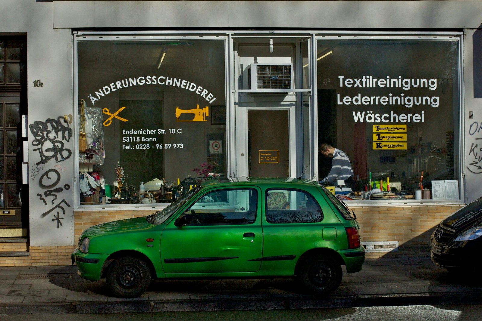A green car parked outside a tailor shop in Bonn, Germany.